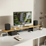 A clean, modern desk with a Mount-It! Extra Wide Monitor Riser with Drawers and Shelf holds a computer monitor showing a waterfall, black speakers, wireless keyboard and mouse, small fan, decorative vase, candle, and desk organizer on a white surface.