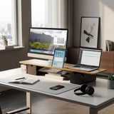 A minimalistic desk setup features the Mount-It! Extra Wide Monitor Riser with Drawers and Shelf, holding a desktop computer, laptop, tablet, notebook, smartphone, wireless headphones, and pen—all neatly organized with city views in the background.