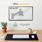 A Mount-It! Single Monitor Wall Mount Arm holds screens 13-32” (75x75/100x100), up to 14.3 lbs, above a desk with a plant, keyboard, mouse, mug, pen, and black mat.