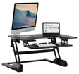 The Mount-It! Standing Desk Converter features a black two-tier design with an ergonomic keyboard tray, supporting an iMac, laptop, and accessories in a dual monitor setup—monitors above and keyboard/mouse below for easy access.