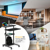 The Mount-It! Height Adjustable Rolling Stand up Desk, in black with locking casters, securely holds a laptop, drink bottle, keyboard, mouse, and backpack—proving its versatile use in auditoriums, offices, or home studies.
