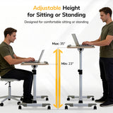 A man uses the Mount-It! Height Adjustable Rolling Laptop Cart, sitting at its 23" height and standing at its 35" max. Text: Adjustable from 23”–35”—ideal for comfort anywhere.