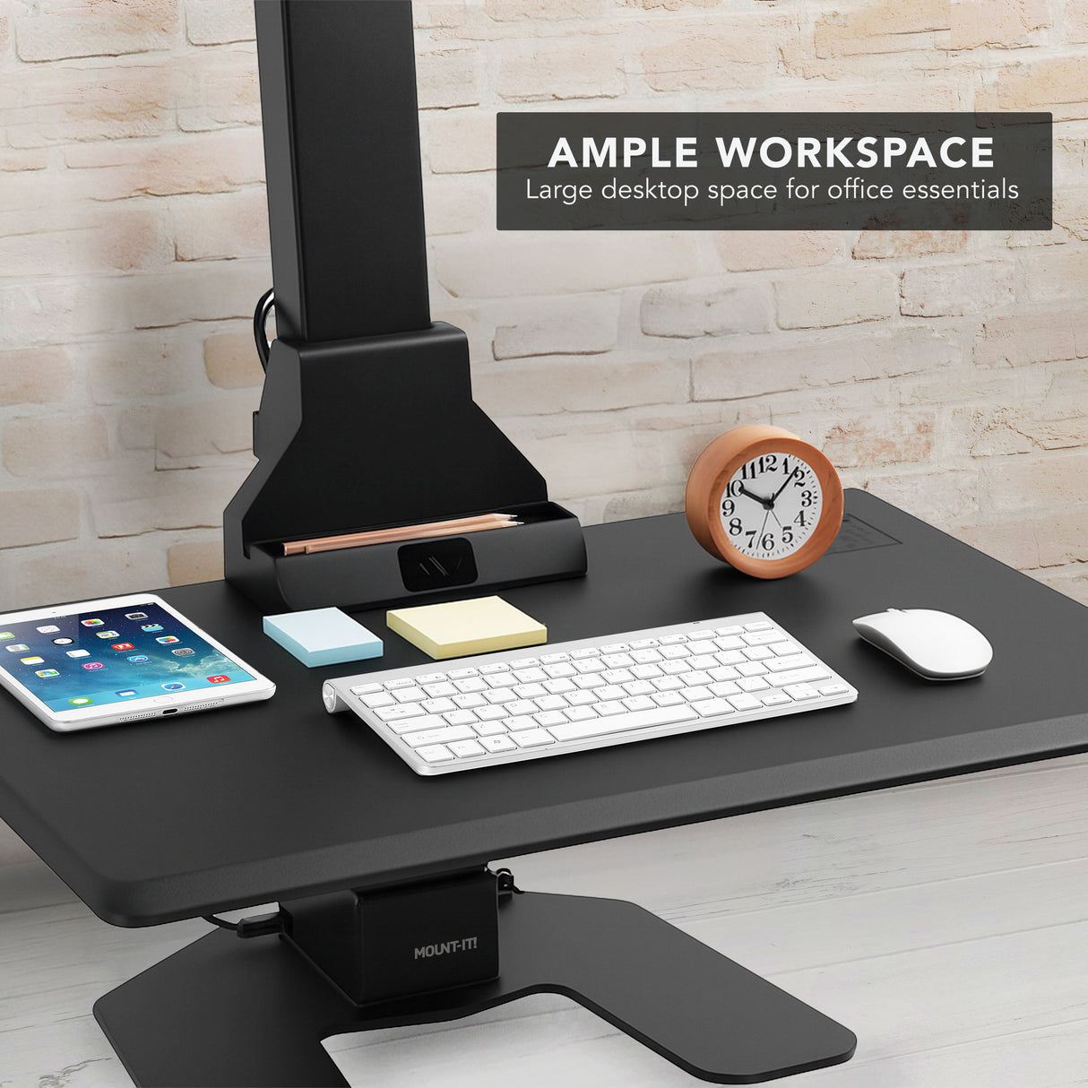 Black adjustable desk converter with office essentials on a light wood floor and stone wall background