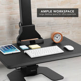 Black adjustable desk converter with office essentials on a light wood floor and stone wall background