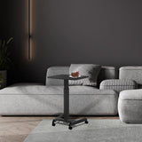 A modern living room with a gray sectional, a tall wall light, and the Mount-It! Height Adjustable Rolling Laptop Desk on wheels holding cake, set against a dark gray wall and light wood flooring.