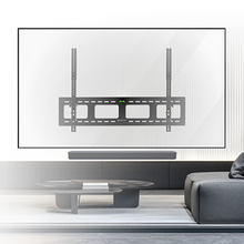 Minimalist living room with a black TV wall mount centered on a white wall, above a long soundbar. A low black coffee table and sectional sofa are in the foreground.