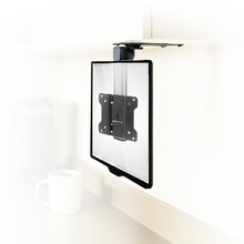 A flat-screen TV wall mount is installed under a white cabinet, with a blurred white mug in the background on a countertop.